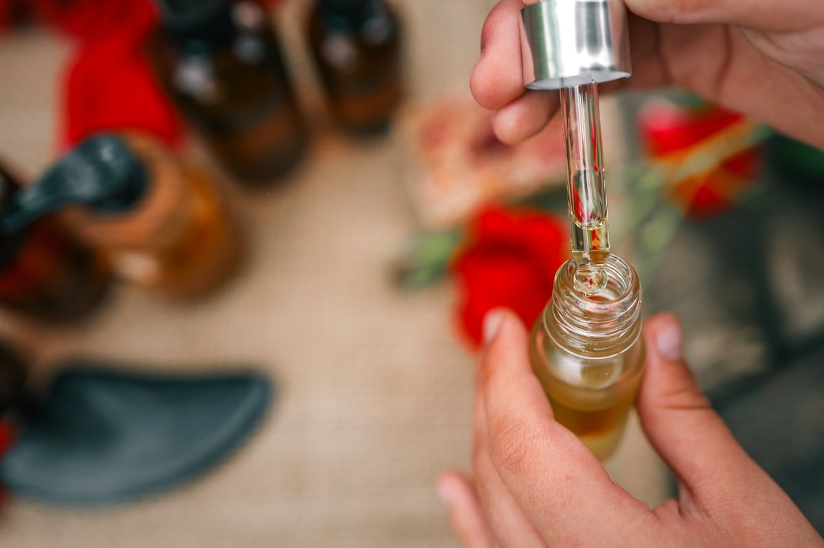 Dropper bottle with golden essential oil surrounded by red rose petals and apothecary jars. Concept of aromatherapy, skincare, and natural beauty products.